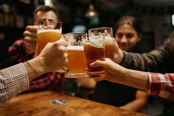Friends toasting with pint glasses of beer at a bar, celebrating together around a wooden table.