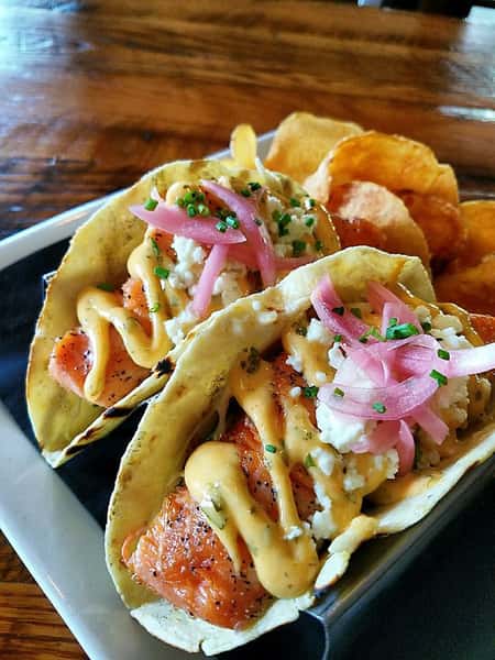 fish tacos with sauce, pickled onions and a side of chips