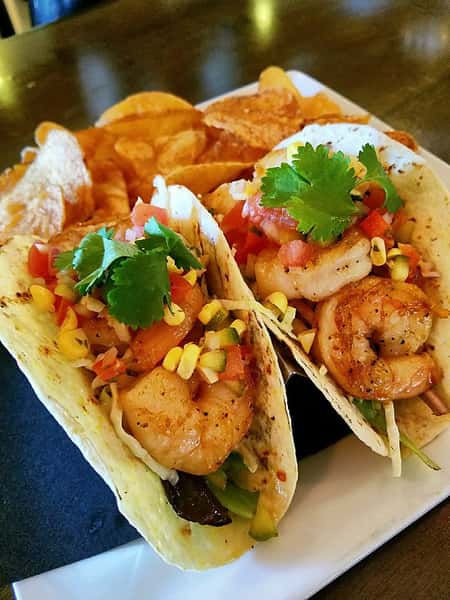 two shrimp tacos with vegetables and a side of chips