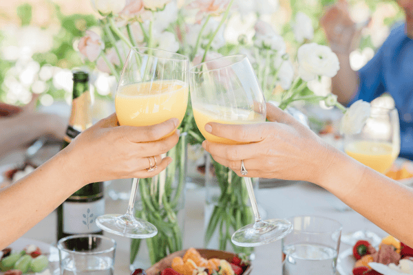 Two hands holding mimosas for a cheers