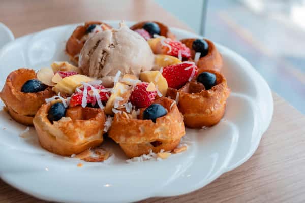 Mini waffles topped with strawberries, blueberries, banana slices, coconut flakes, and a scoop of ice cream.
