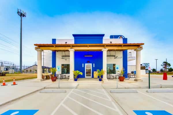 Front view of a bright blue and white restaurant with tall columns, patio seating, and marked accessible parking spaces.