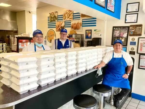 Three staff members at Papa Gyros stand proudly behind a long counter stacked with takeout containers, showcasing preparation for a large order or community event.