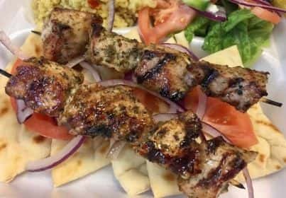 Grilled chicken souvlaki skewers served over pita bread with sliced tomatoes, red onions, and a side salad.
