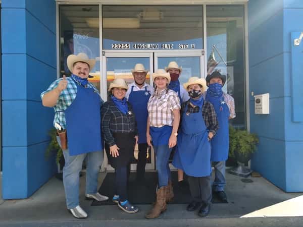Team of employees wearing blue aprons, plaid shirts, and cowboy hats posing outside Pappa Gyros restaurant in Katy, Texas.