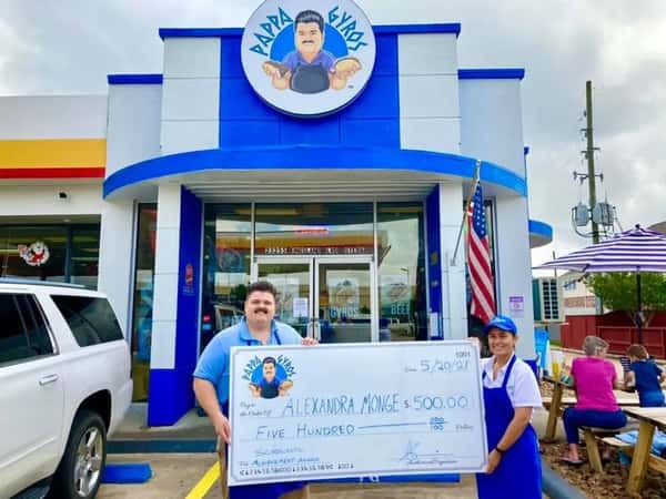 Two people stand smiling outside Papa Gyros holding a giant $500 scholarship check awarded to Alexandra Monge.