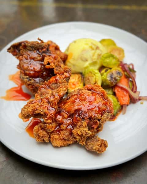 Fried chicken thighs, served with mashed potatoes, vegetables, and hot sauce gastrique