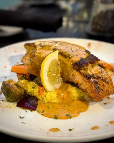 blackened salmon paired with stuffed, breaded crabmeat. It's served with creamy polenta, seasonal vegetables, and finished with a rich creole cream sauce