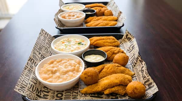 Two trays of fried fish, hush puppies, coleslaw, baked beans, and a small cup of tartar sauce.