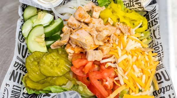 Salad with diced chicken, sliced cucumbers, pickles, tomatoes, yellow peppers, and shredded cheddar cheese on a bed of lettuce.