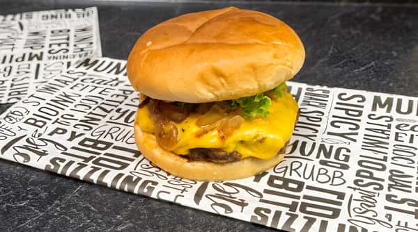 Cheeseburger with melted yellow cheese, caramelized onions, and lettuce on a bun, resting on patterned paper.