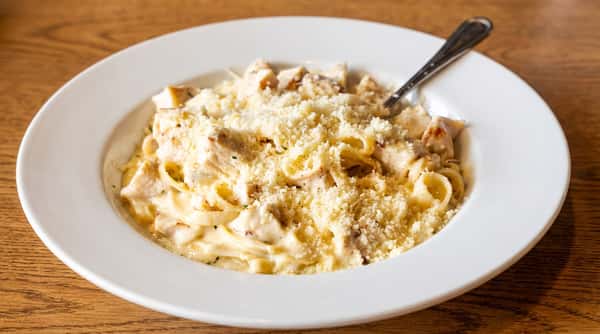 Fettuccine Alfredo with chicken and a generous topping of grated Parmesan cheese, served on a white plate with a spoon.