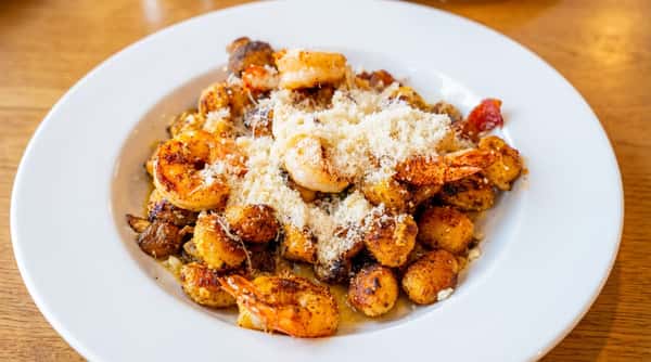 Seared shrimp and golden brown gnocchi topped with grated cheese on a white plate.
