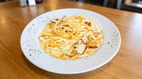 Fettuccine Alfredo with grilled chicken pieces in a creamy white sauce on a white plate.