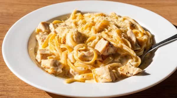 Fettuccine Alfredo with diced chicken and grated parmesan cheese on a white plate in natural light.