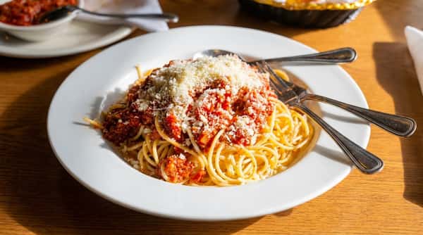 Spaghetti with meat sauce and grated Parmesan cheese on a white plate, with a fork.