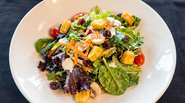 Garden salad with mixed greens, cherry tomatoes, sliced olives, mushrooms, shredded carrots, and croutons, dressed with ranch.