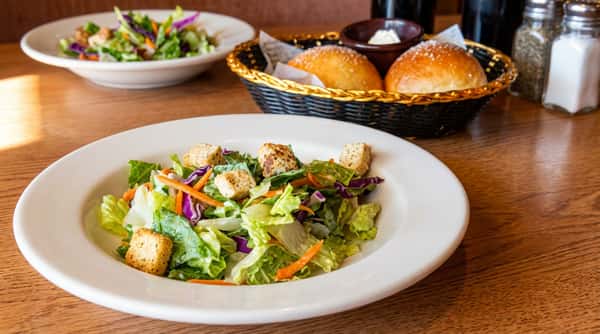 Side salad with croutons and a basket of dinner rolls with butter on a wooden table.