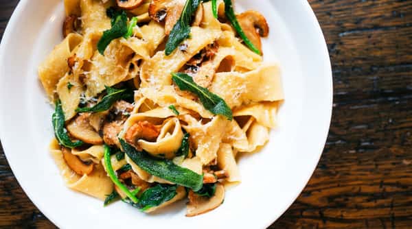 Pappardelle pasta with mushrooms, green herbs, and grated cheese on a white plate.