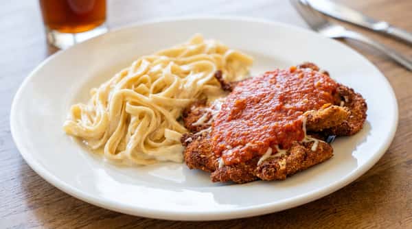 Chicken Parmesan with red sauce and melted cheese, served with creamy fettuccine on a white plate.