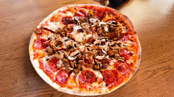 Pizza with pepperoni, sausage, and mushrooms on a wooden table.
