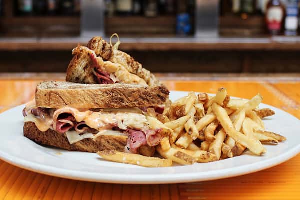Photo of the Reuben sandwich, cut in half and served with fries.