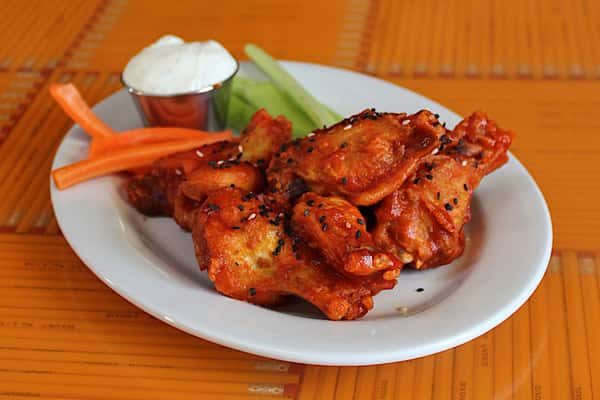 Photo of Confit Chicken Wings, tossed in Sriracha-Honey sauce, topped with sesame seeds and plated with carrot sticks, celery and ranch.