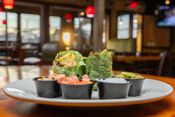 Plant-based burrito wrap stuffed with roasted vegetables and black beans, accompanied by house-made salsa, guacamole, and sour cream in a warm, inviting Mexican dining setting.