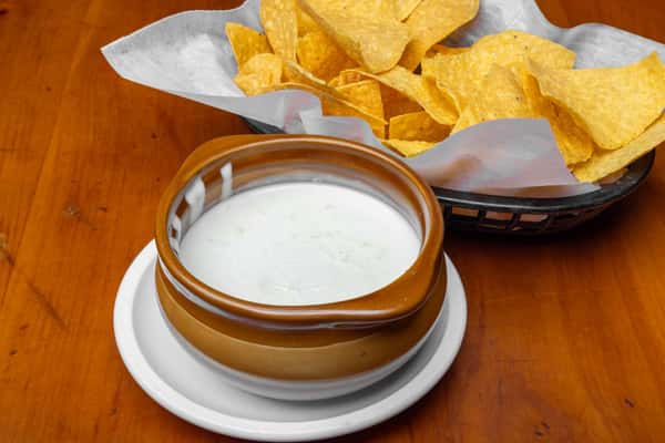 Crispy tortilla chips served with a bowl of creamy white queso dip, a classic Mexican restaurant appetizer presented in a rustic ceramic dish.