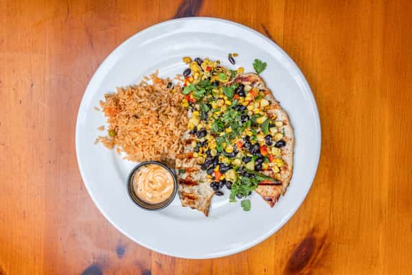 Grilled chicken breast topped with roasted corn and black bean salsa, fresh cilantro, and diced peppers, served with Mexican rice and chipotle cream sauce, showcasing a colorful and flavorful Tex-Mex entrée.