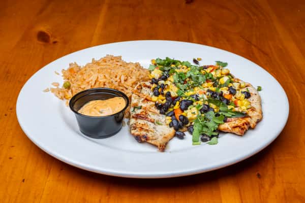 Grilled chicken breast topped with black beans, roasted corn salsa, and fresh cilantro, served with Mexican rice and a creamy chipotle sauce, capturing a fresh and flavorful Tex-Mex entrée on a warm wooden table.