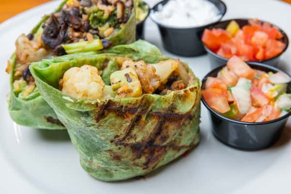Grilled spinach tortilla wraps filled with roasted cauliflower, zucchini, black beans, and sautéed vegetables, served with fresh pico de gallo and sour cream, highlighting a flavorful vegetarian Tex-Mex option with vibrant colors and bold ingredients.