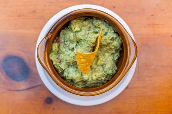 Close-up of chunky house-made guacamole topped with a crisp tortilla chip, served in a rustic bowl at Tijuana Joe's.