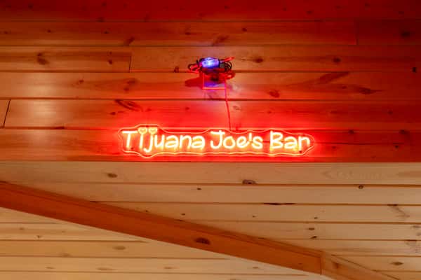 Red neon "Tijuana Joe's Bar" sign mounted on rustic wood paneling, highlighting the lively Mexican bar ambiance.