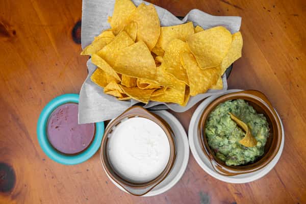 Fresh tortilla chips served with creamy white queso, house-made guacamole, and red salsa at a Tex-Mex restaurant.