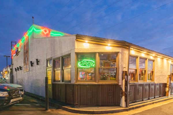 Mexican restaurant exterior at dusk with glowing neon "Open" sign and colorful rooftop lights, welcoming guests to a lively neighborhood cantina.