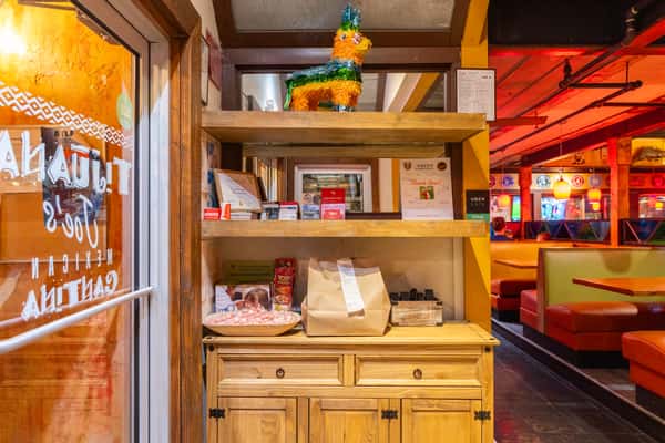 Host stand with wooden shelving, colorful piñata decor, and warm lighting inside Tijuana Joe's Mexican restaurant, showcasing a vibrant Tex-Mex atmosphere.