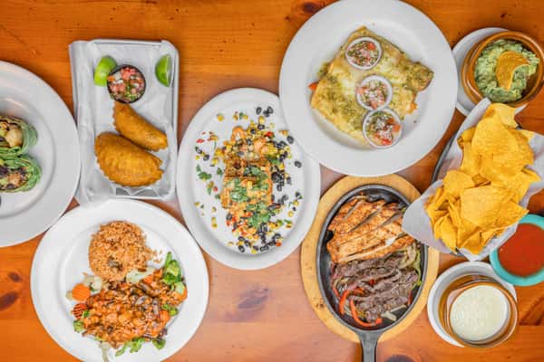 Overhead view of a Tex-Mex feast featuring fajitas, enchiladas, Mexican rice, empanadas, chips with queso and guacamole at Tijuana Joe's restaurant.