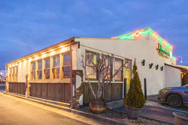 Exterior of Abuelos Mexican restaurant at dusk, featuring warm interior lighting, colorful neon signage, and a cozy Southwestern-style facade with large windows and rustic details.