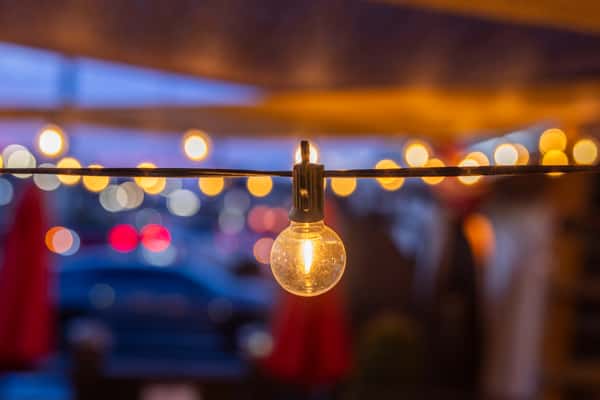 Close-up of glowing string lights on a Mexican restaurant patio at night, creating a warm, inviting ambiance with soft bokeh city lights in the background.