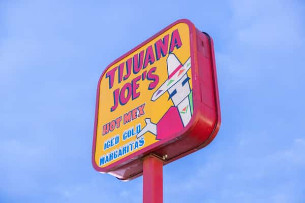 Tijuana Joe's roadside sign featuring bold colorful lettering with "Hot Mex" and "Iced Cold Margaritas" against a clear blue sky, highlighting a vibrant Tex-Mex restaurant known for margaritas and authentic Mexican cuisine.
