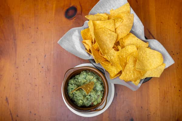 Crispy tortilla chips served with house-made guacamole in a rustic bowl, perfect for sharing at a festive Mexican cantina.