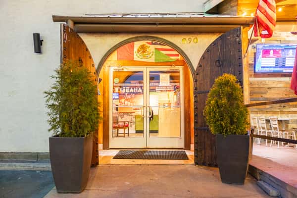 Tijuana Joe's Cantina entrance with rustic wooden doors, Mexican flag décor, and warm ambient lighting, capturing the inviting atmosphere of a festive Tex-Mex restaurant with outdoor patio seating.