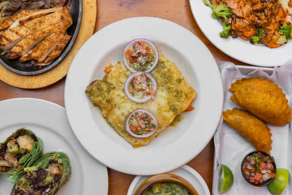 Cheese enchilada with green salsa and pico de gallo, paired with golden fried empanadas, fresh guacamole, and sizzling fajitas for a vibrant Tex-Mex dinner spread.