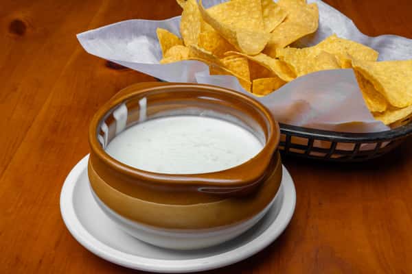 Crispy tortilla chips served with creamy white queso dip in a rustic bowl, showcasing a classic Mexican restaurant appetizer perfect for sharing in a casual cantina setting.
