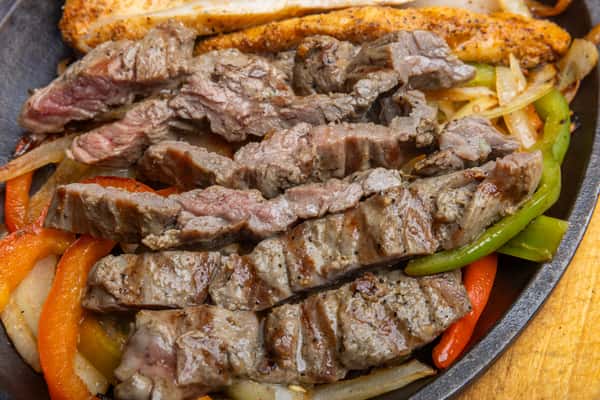 Juicy grilled steak fajita strips with sautéed bell peppers and onions on a sizzling cast iron skillet, showcasing authentic Tex-Mex flavors.
