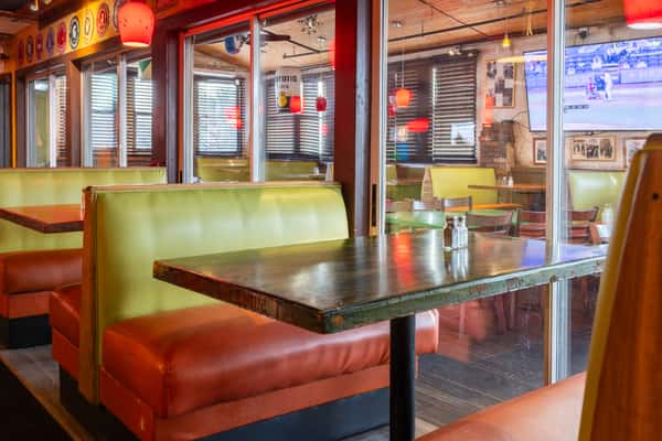 Cozy booth seating with green and red cushions, wood tables, and glowing red pendant lights inside Tijuana Joe's Tex-Mex restaurant dining area.