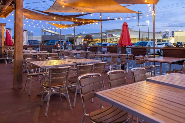 Spacious outdoor patio dining area with string lights, shaded seating, and wooden tables, creating a relaxed atmosphere at a vibrant Mexican restaurant.