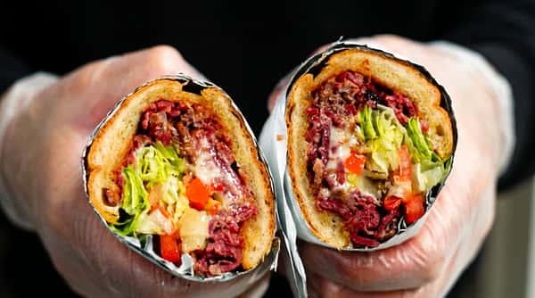 Two halves of a large hoagie sandwich filled with deli meat, melted cheese, lettuce, tomatoes, and peppers, wrapped in foil.