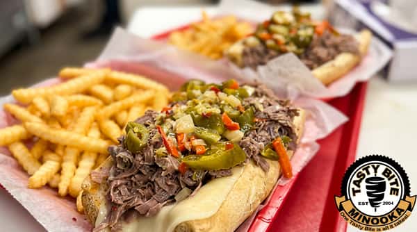 Two Italian beef sandwiches with melted cheese, pickled vegetables, and a side of crinkle-cut fries on red trays.